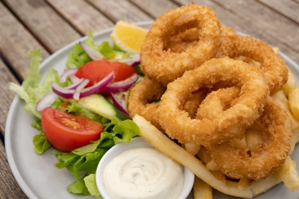 A Plate of Food With Squid Rings, French Fries, and a Salad on a Wooden Table — Mulgrave Seafoods In Earville, QLD
