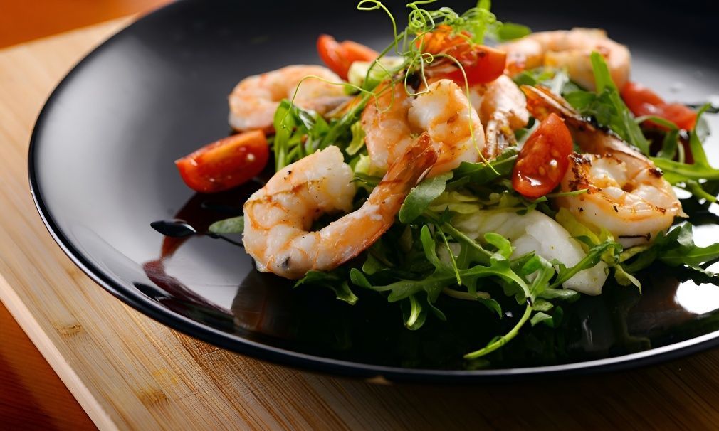 A Black Plate Topped With Shrimp and Tomatoes on a Wooden Table — Mulgrave Seafoods In Bungalow, QLD