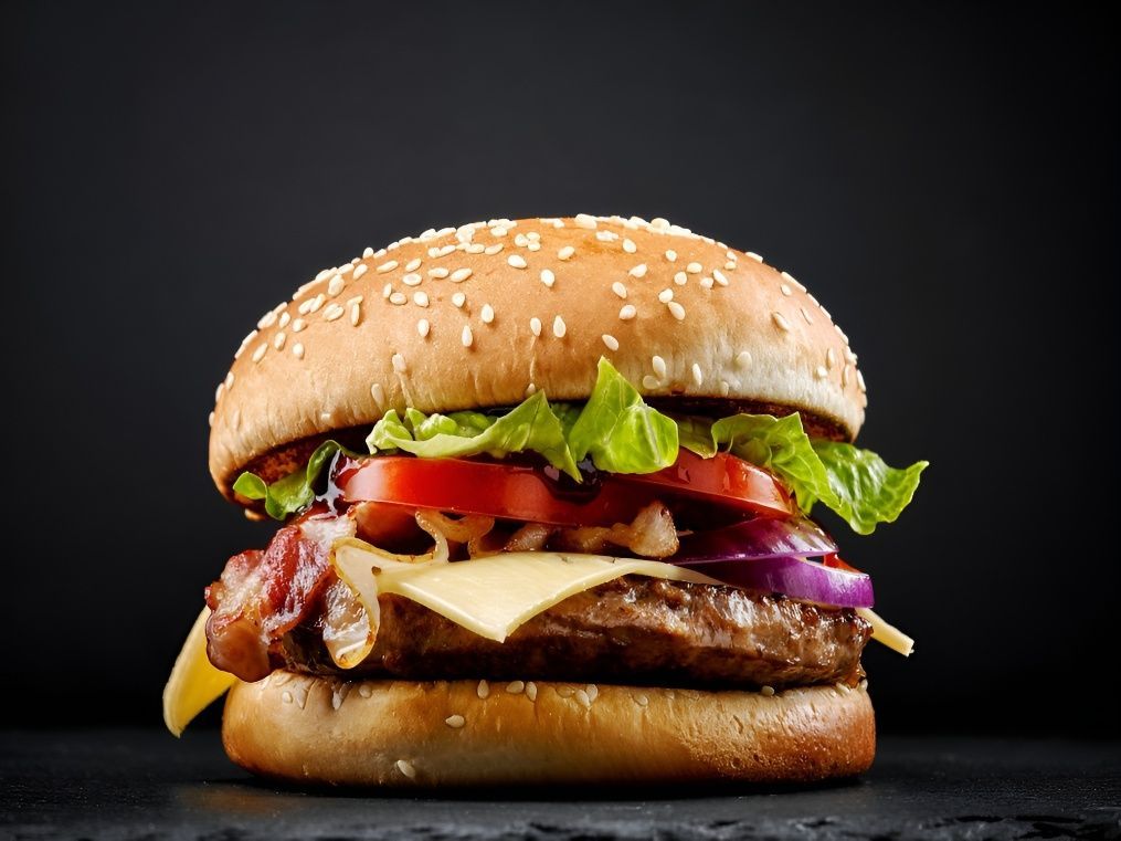 A hamburger with cheese, lettuce, tomatoes, onions and bacon on a sesame seed bun — Mulgrave Seafoods In Portsmith, QLD