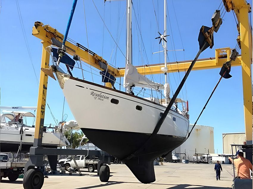A White Sailboat is Being Lifted by a Yellow Crane — Mackay Marine Services in Mackay, QLD
