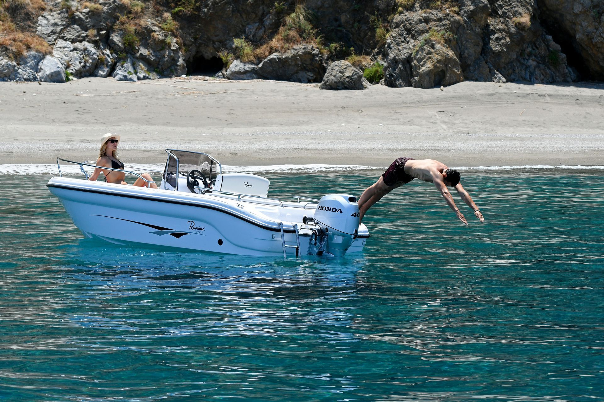 Man Diving From Boat Into Blue Water, Woman on Board. Beach in the Background — TJM Rockhampton in Rockhampton City, QLD