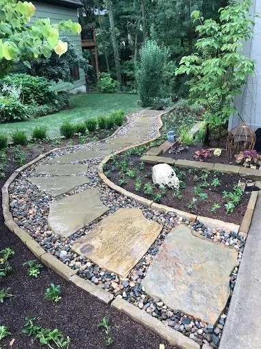 A stone walkway leading to a garden in a backyard.
