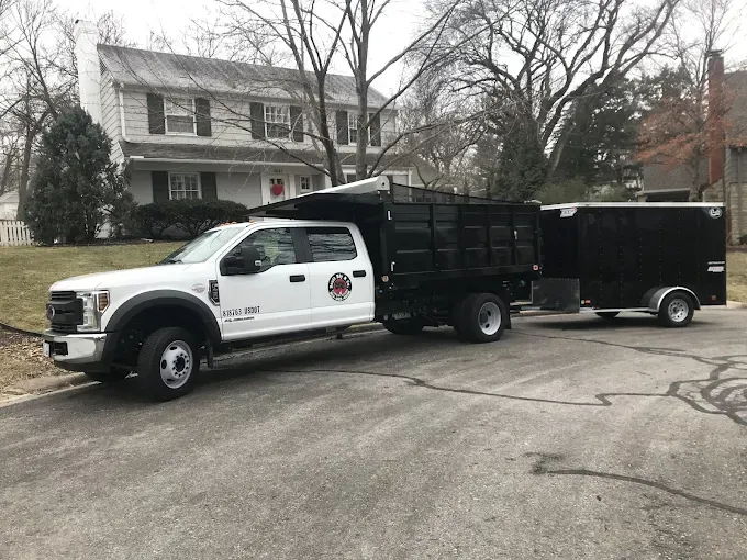 A white truck with a black trailer attached to it is parked in front of a house.