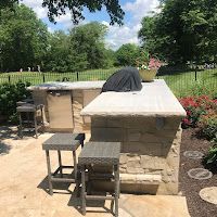 A large outdoor kitchen with a grill and stools in a backyard.