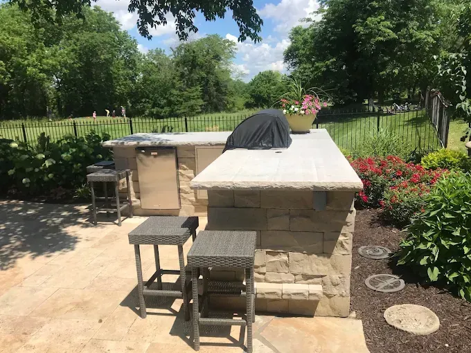 A large outdoor kitchen with a grill and stools in a backyard.