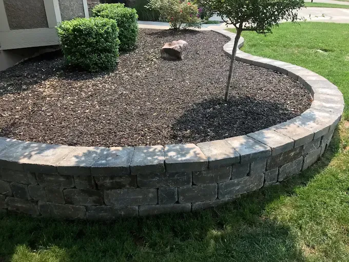 A brick wall surrounds a circular planter in a yard.