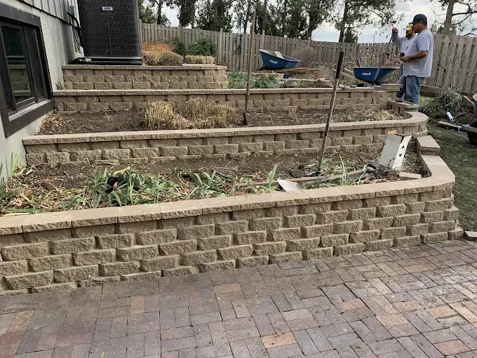 A man is standing next to a brick wall in a garden.