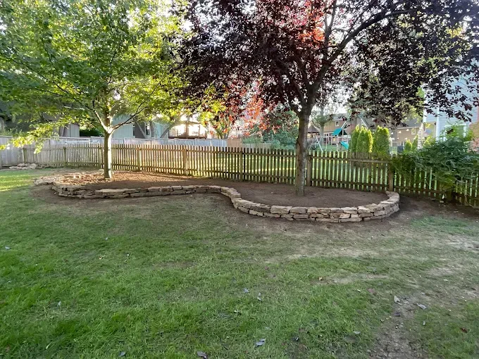 A backyard with a fence and a tree in the middle of it.