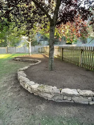 A stone wall is surrounding a tree in a backyard.