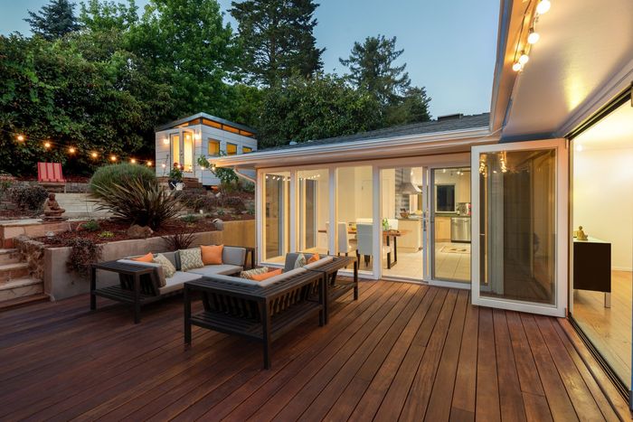 A large wooden deck with a couch and chairs on it in front of a house.