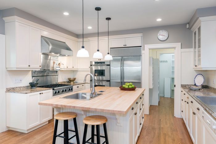 A kitchen with white cabinets , wooden counter tops , stainless steel appliances , and a large island.