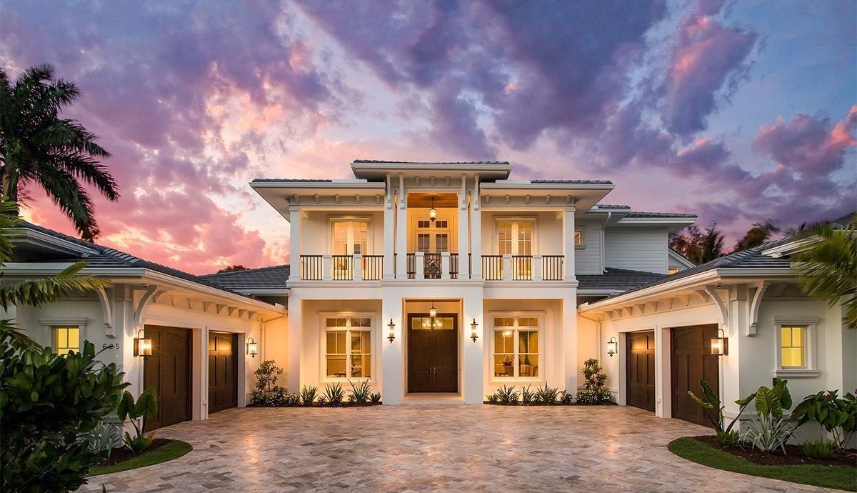 A large white house with a driveway and palm trees in front of it.