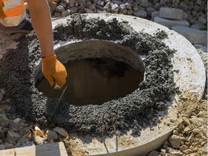 A man is pouring concrete into a manhole cover.