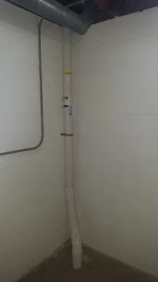 A white PVC pipe runs vertically along the corner of an interior wall, extending from the floor to the ceiling.