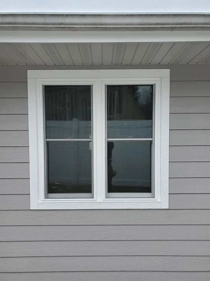 White-framed window with two panes, on a gray horizontal siding wall.