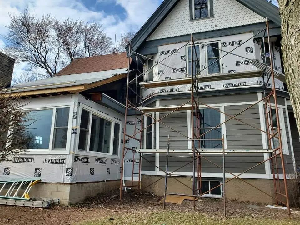 House exterior under construction, scaffolding, gray siding, white trim, blue sky.