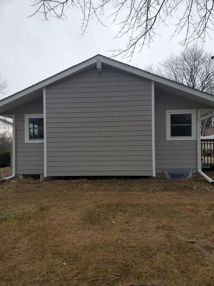 Gray house exterior with two windows and a brown yard.