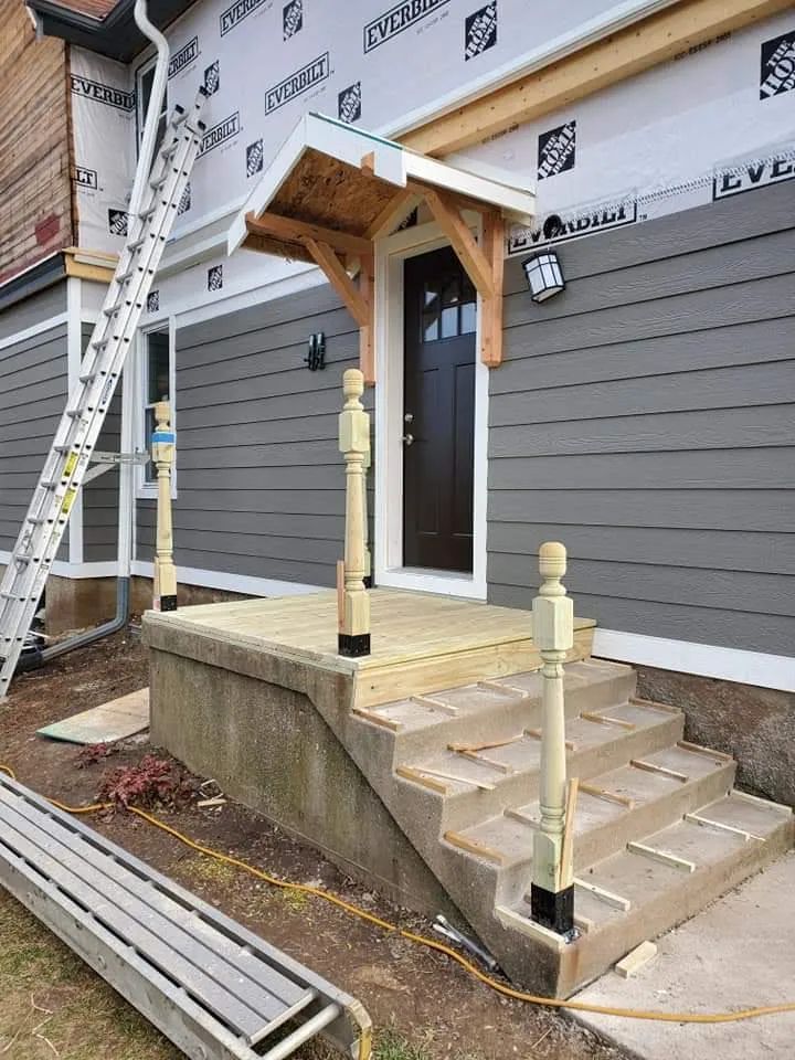 House with porch and steps under construction; gray siding, wooden details. Ladder leaning against the wall.