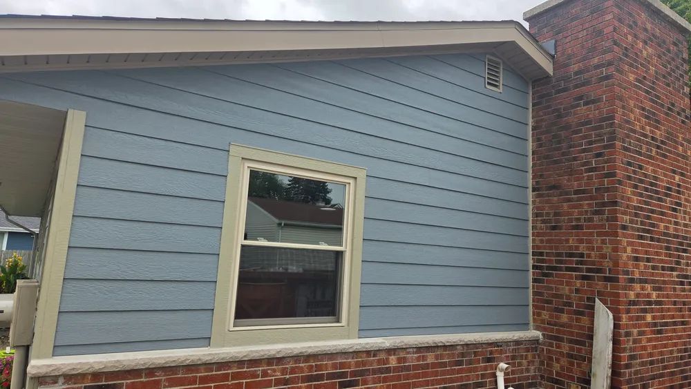Blue siding on a house with a brick chimney and window; beige trim.