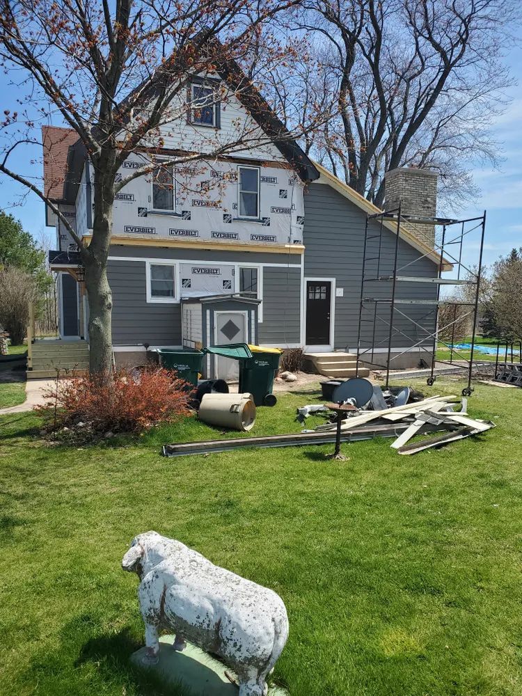 House under construction with grey siding, scaffolding, and yard with sheep statue.