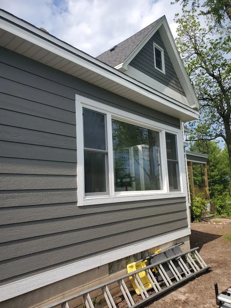 Gray siding with white trim, a large window, and a ladder against the side of a house.