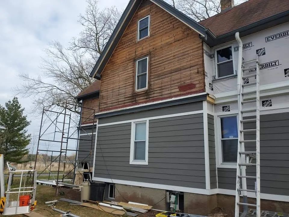 House exterior undergoing renovation: gray siding installed, old wood exposed. Scaffolding, ladder present.
