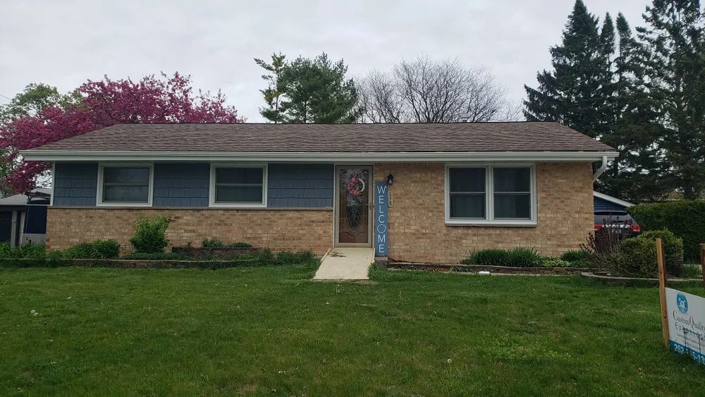 Ranch style house with brick and blue siding, green lawn, and brown roof. House number