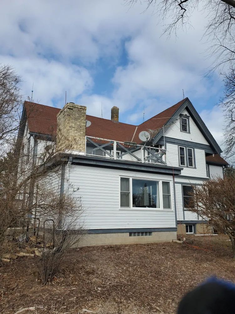 White house with brown roof and chimney, blue sky, and sparse trees.