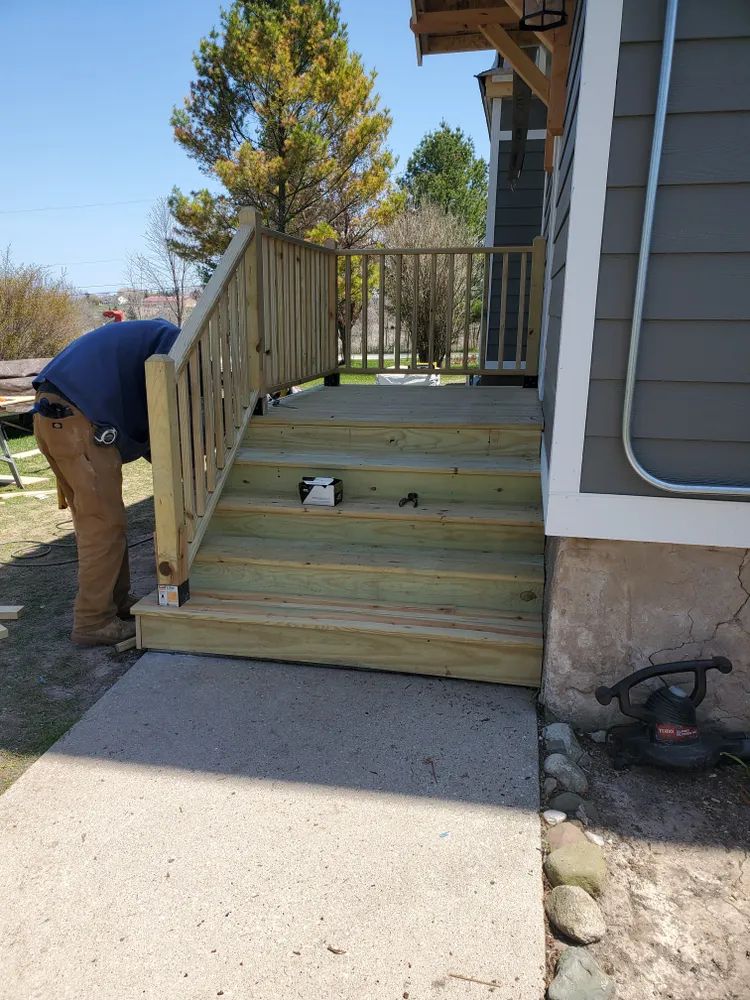 Person building wooden stairs attached to a house with a concrete walkway.