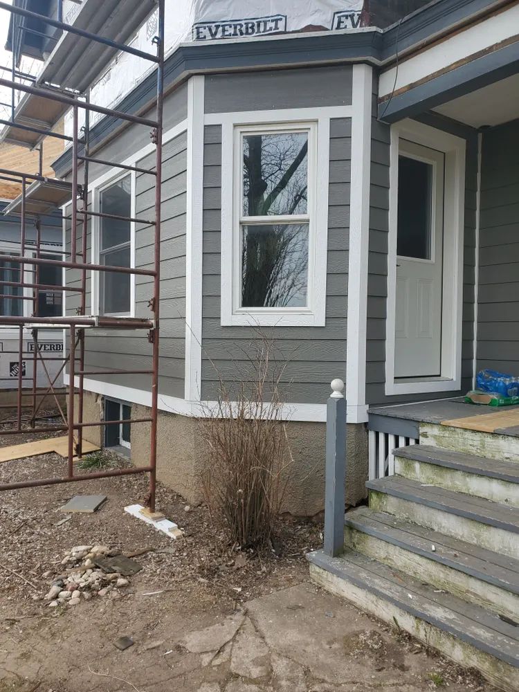 Gray house exterior with white trim, bay window, front door, and porch steps.