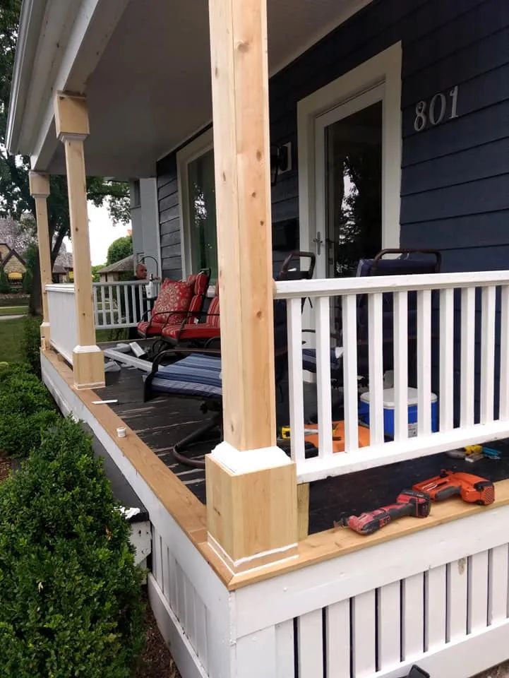 Porch with unfinished wooden columns, white railing, and blue siding. Tools on the floor.