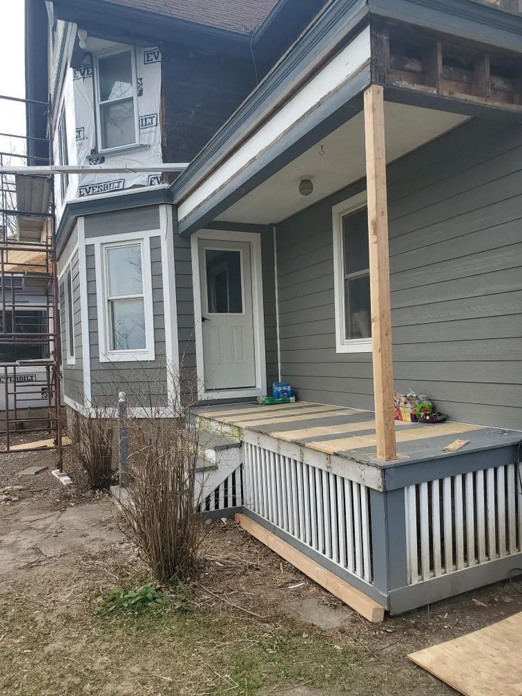 Gray house exterior with porch, steps, and siding under construction.