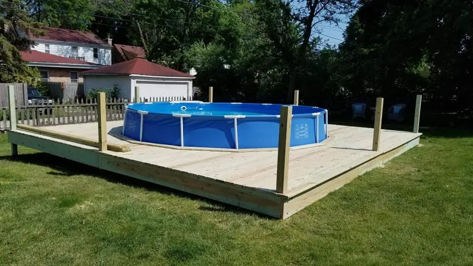 Blue above-ground pool on a wooden deck in a grassy yard.
