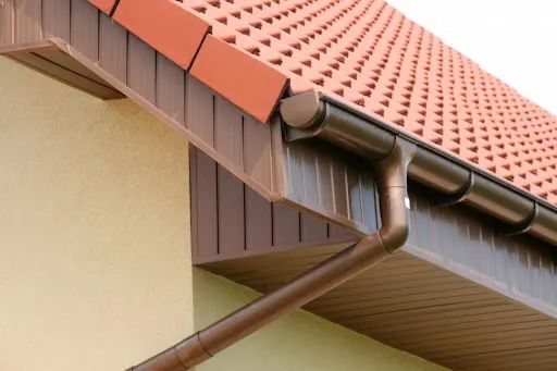 Brown guttering on a house with a red tiled roof and beige walls.