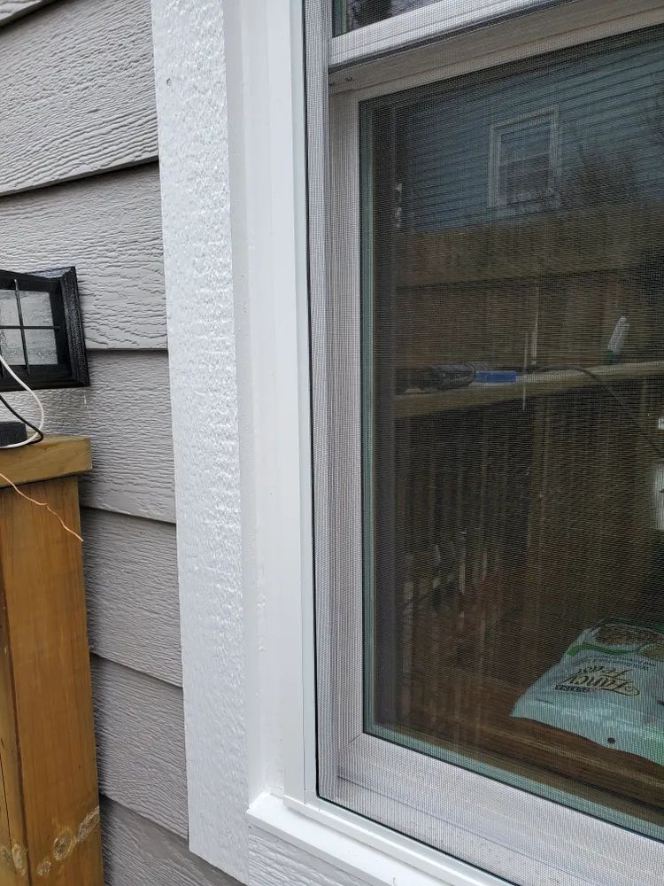 White window frame next to gray siding, with a small black light fixture on a wood surface.
