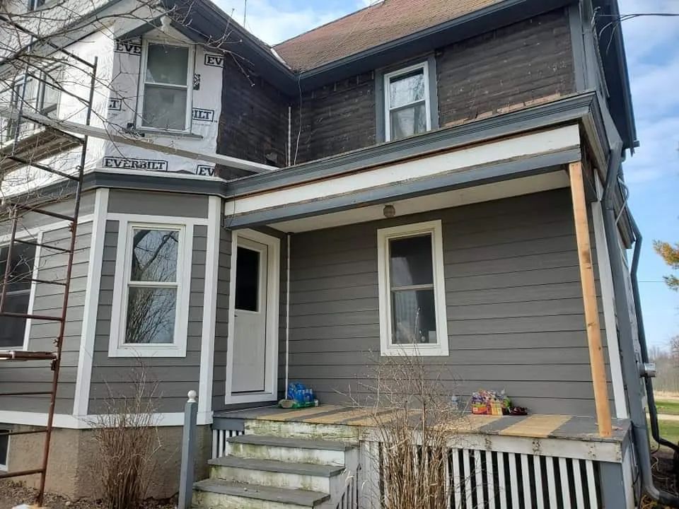 Two-story house with gray siding, white trim, and a porch under construction. Scaffolding is visible.
