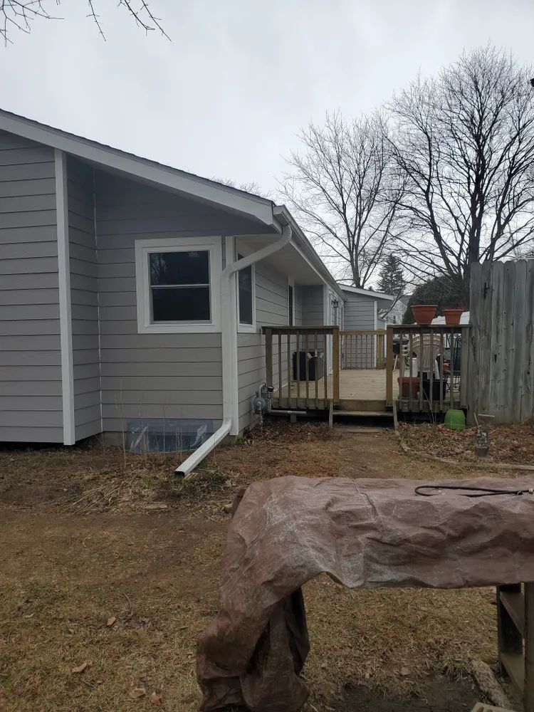 Gray house with a deck in a backyard under an overcast sky.