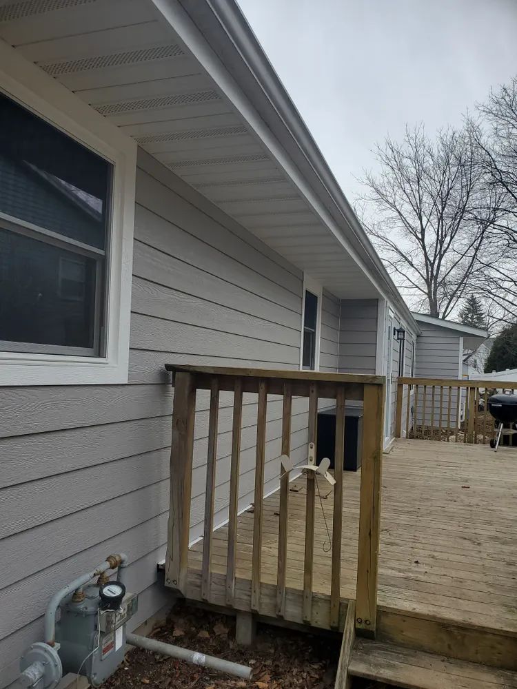 Exterior view of a house with gray siding, white trim, and a wooden deck.