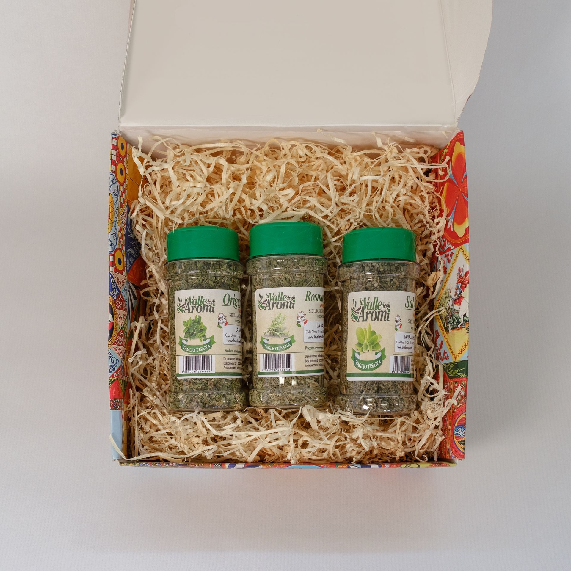 Confezione regalo aperta con tre vasetti e due bottigliette di conserve su un letto di carta sminuzzata.