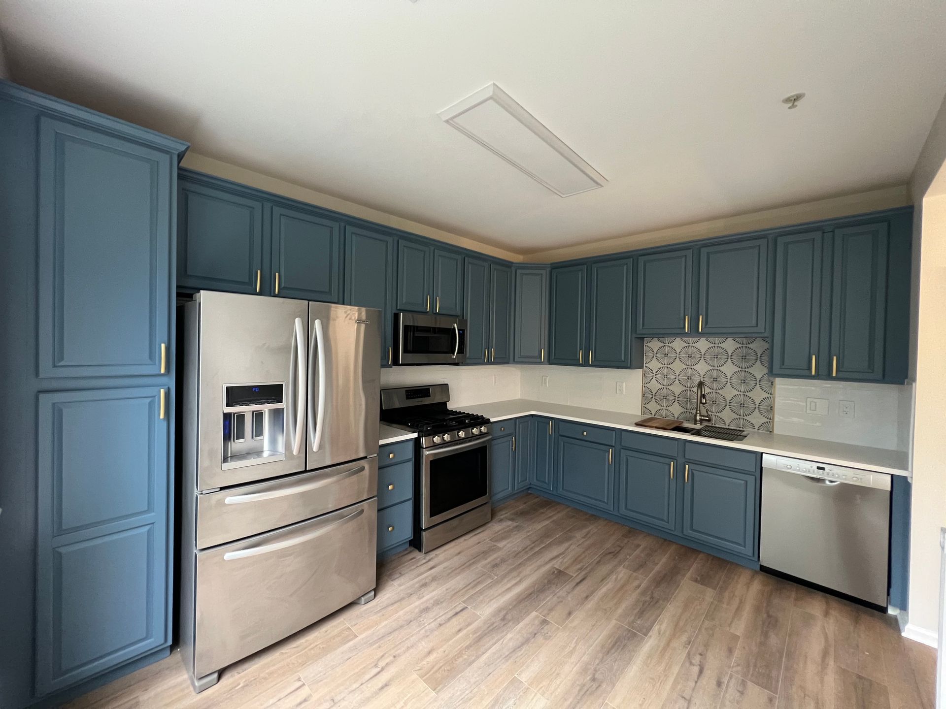 Blue kitchen cabinets with stainless steel appliances on wood-look flooring.