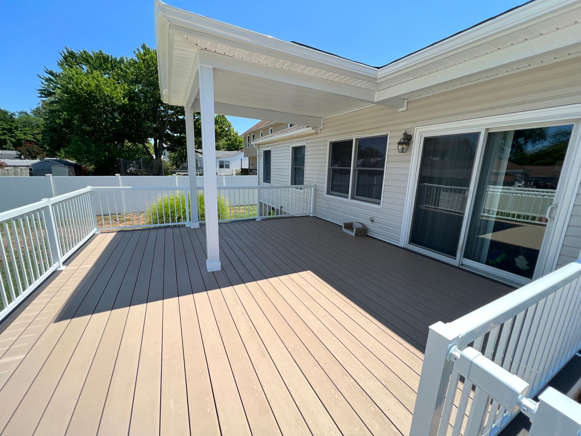 A spacious outdoor deck with white railing and a covered section, attached to a light-colored house.