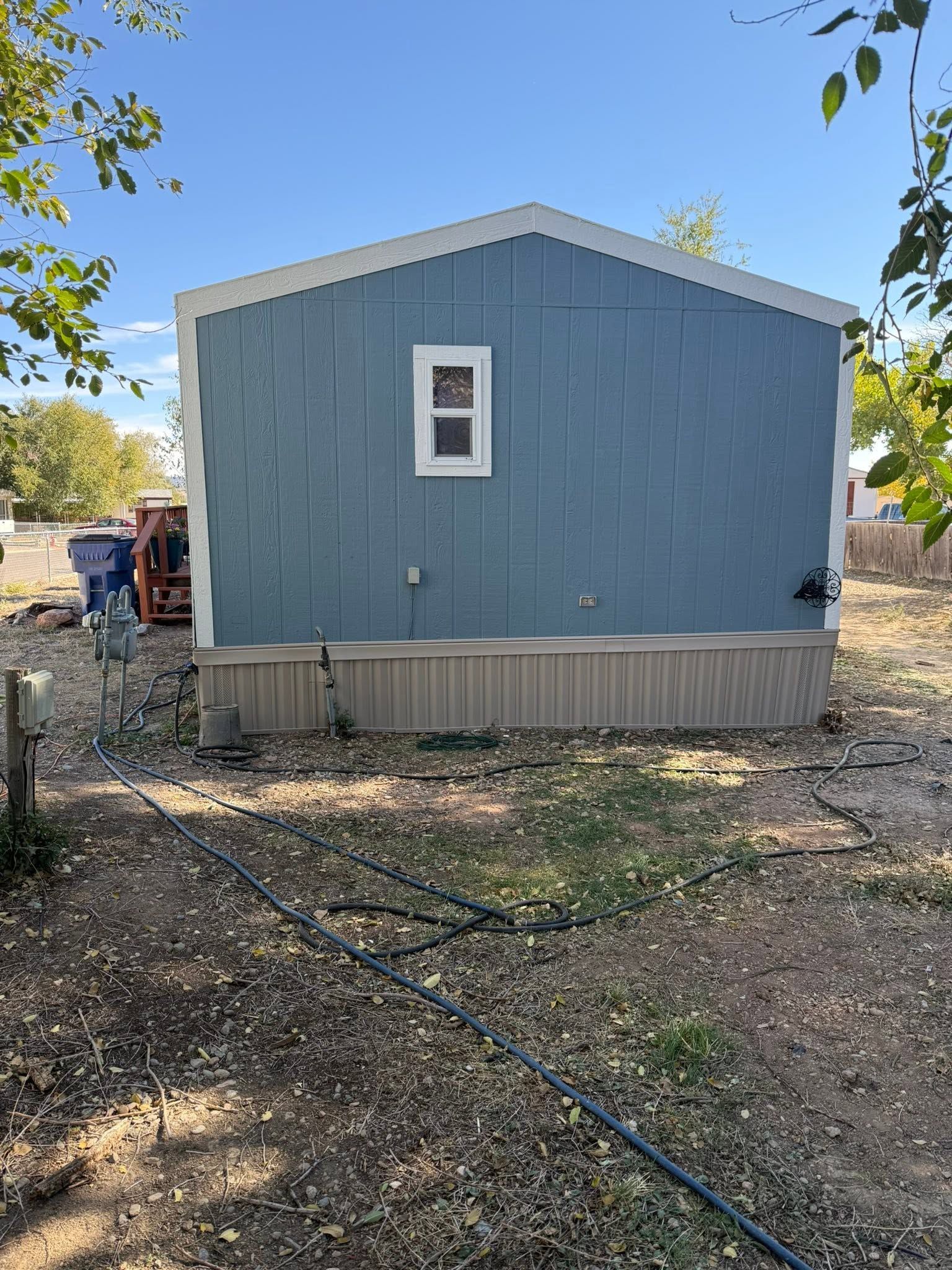 Blue mobile home with a small window, set on a dirt lot under a clear sky.