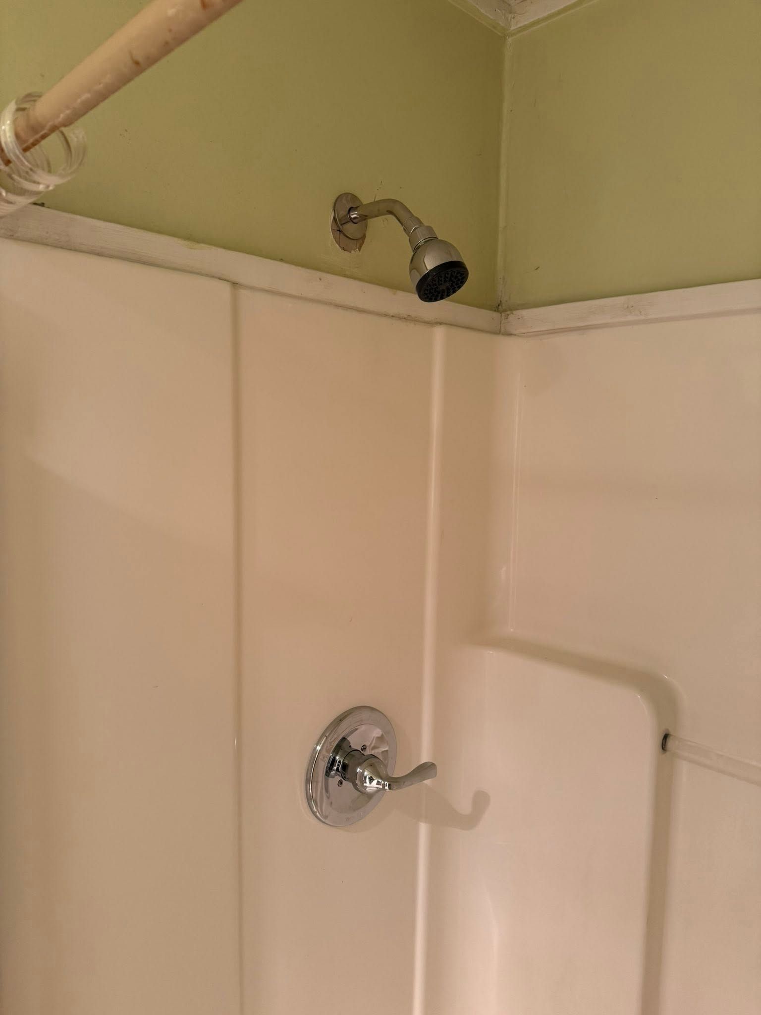 Empty shower stall with beige walls, chrome showerhead, and white trim under a green ceiling.