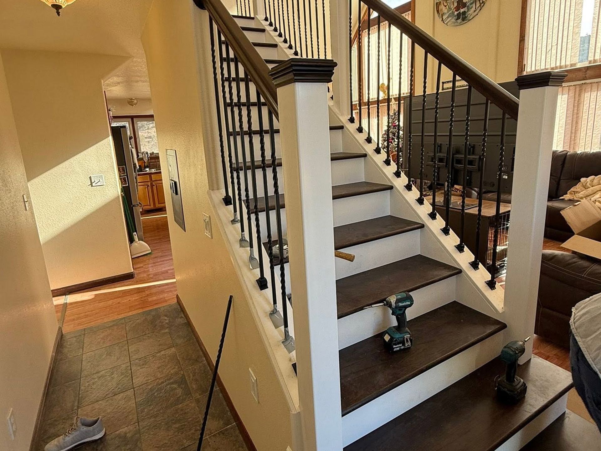 Indoor staircase with black railings and white steps, two cordless drills on the lower stairs.