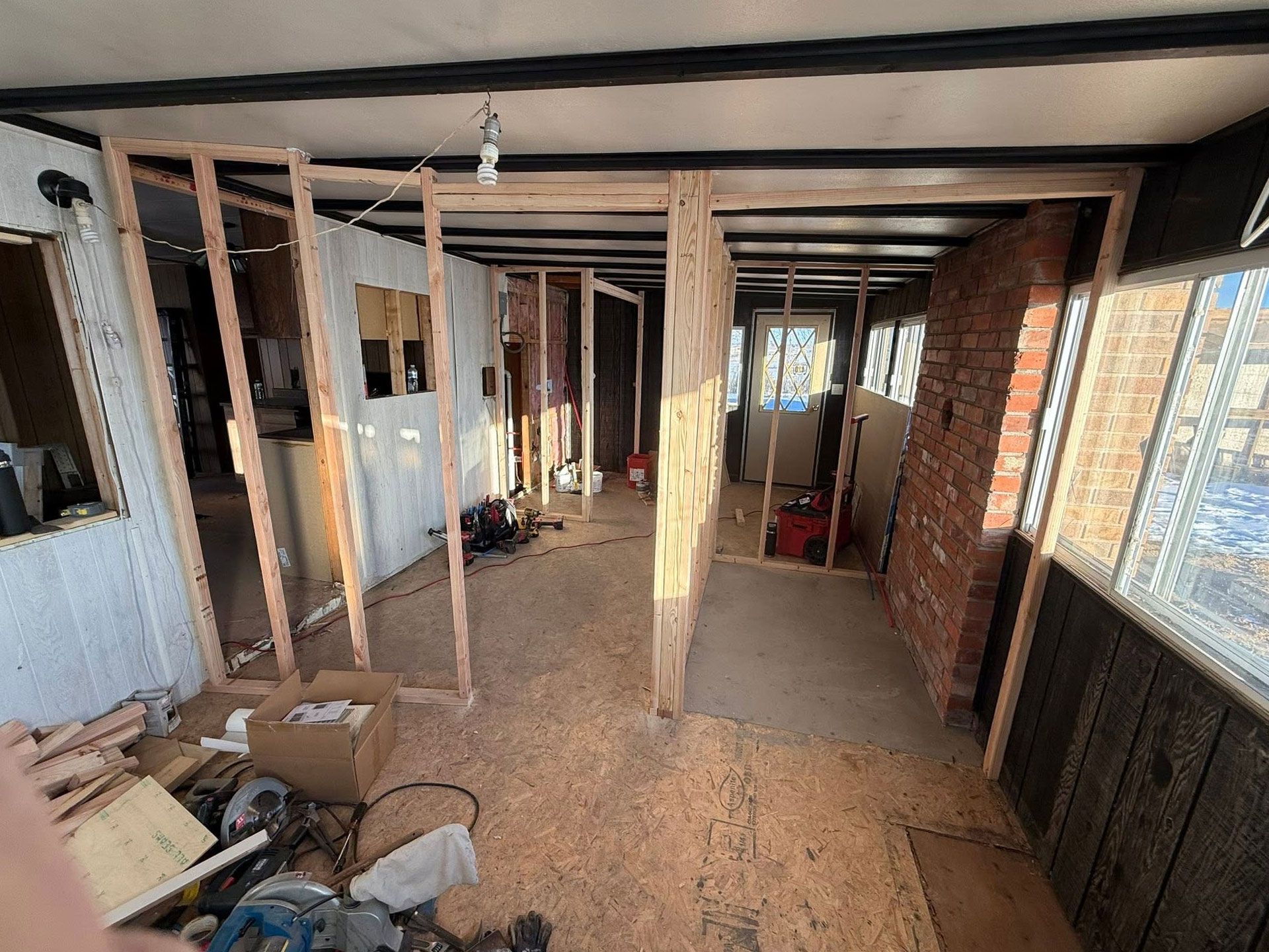 Interior of an unfinished room with exposed framing, brick wall, and debris on the floor
