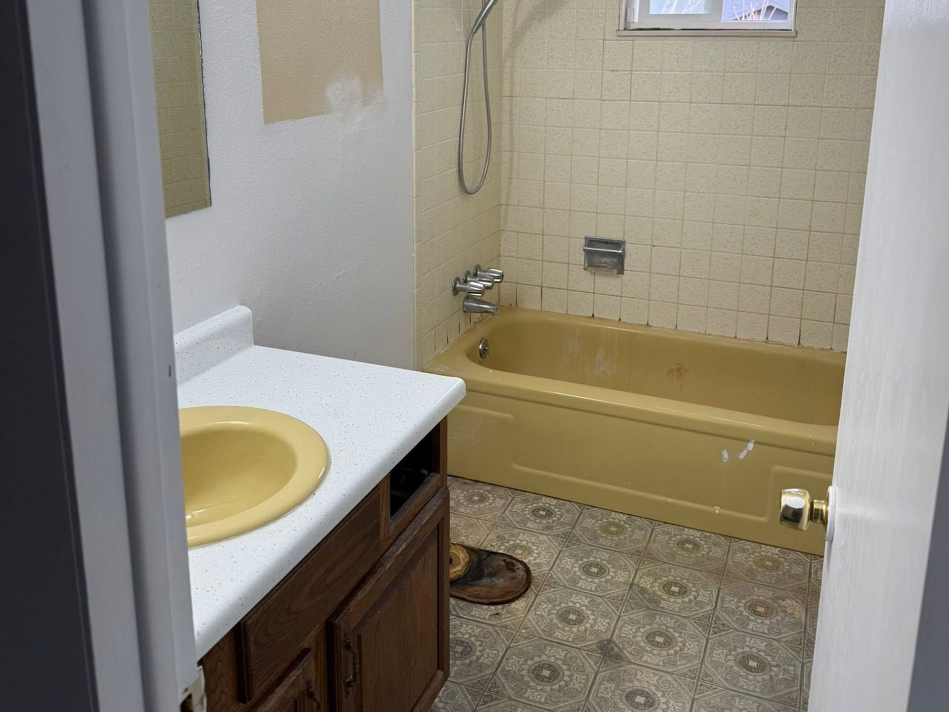 Small bathroom with a sink, toilet, and yellow bathtub against cream tile walls.