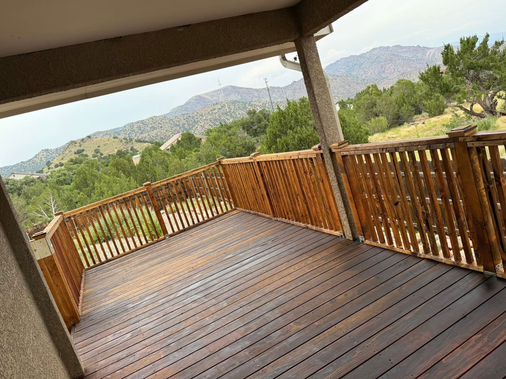 Covered wooden deck with railing overlooking a mountainous, tree-lined landscape