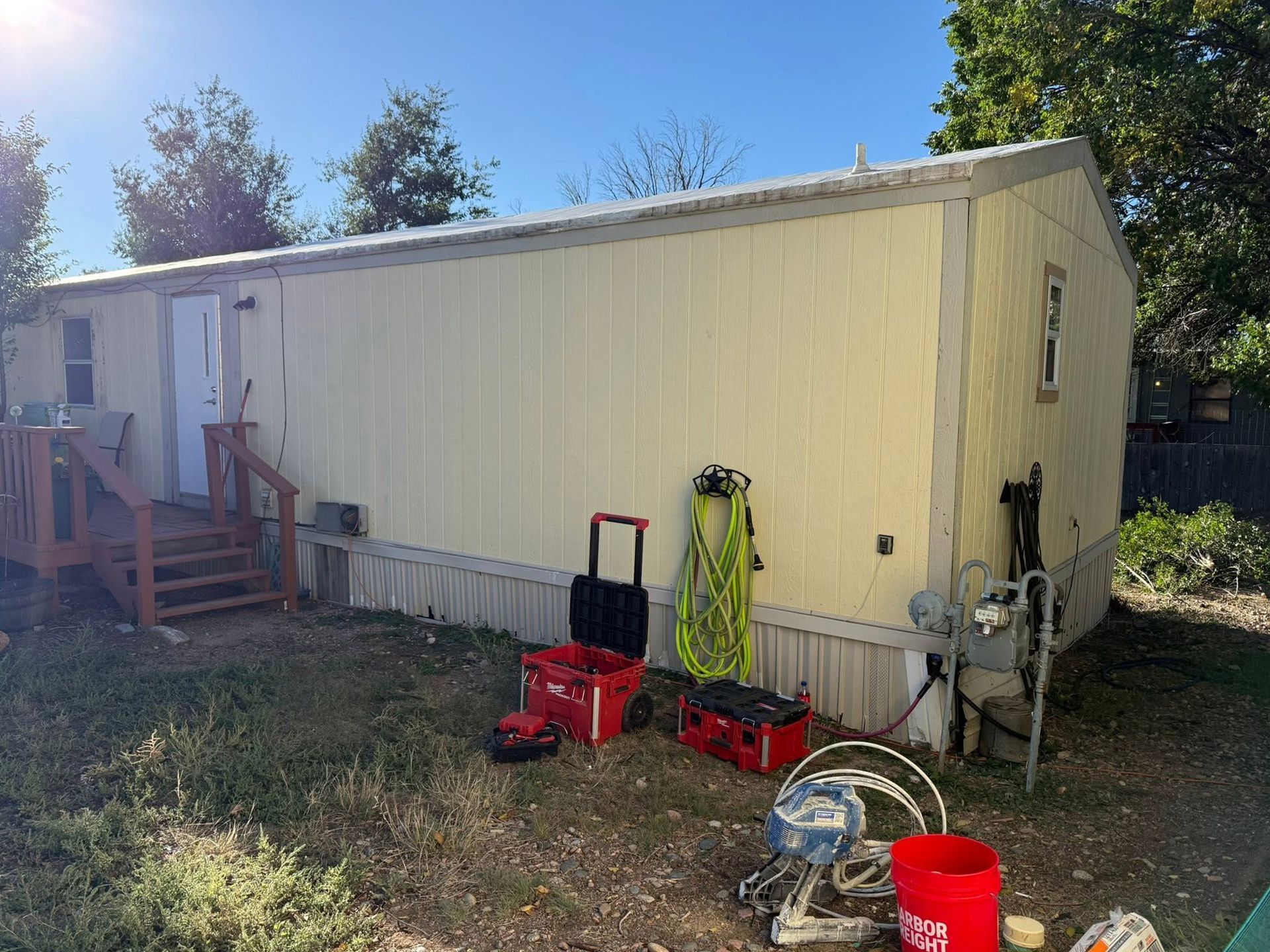 Yellow mobile home exterior with tools and equipment scattered on the grass in bright sunlight