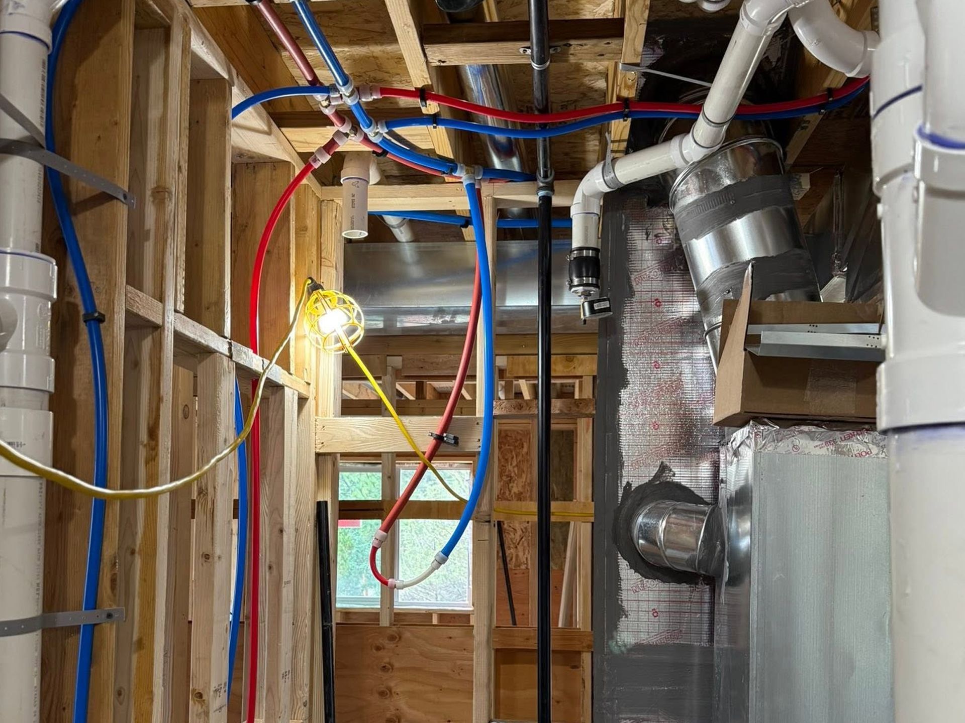 Exposed home framing with hanging red and blue cables, ductwork, and HVAC equipment in a basement