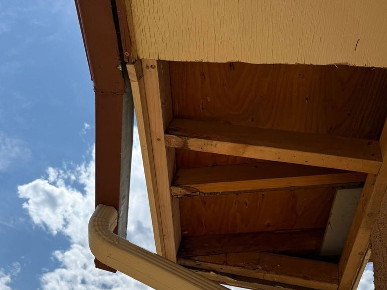 Upward view of a wooden roof eave against a blue sky with clouds
